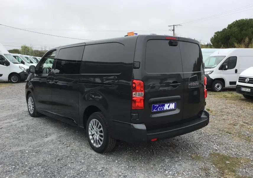 Vue 3/4 arrière droite d’un Peugeot Expert cabine approfondie gris titane avec vitres arrière teintées et feux rouges visibles.