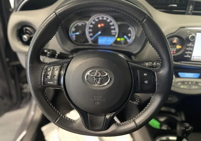 Vue rapprochée du volant en cuir noir de la Toyota Yaris hybride 2020, avec commandes intégrées et tableau de bord flou en arrière-plan.