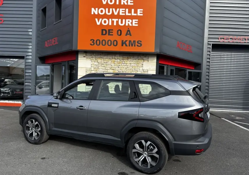 SUV Dacia Bigster gris foncé vu de profil côté gauche, avec barres de toit noires et feux arrière LED distinctifs.