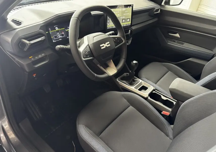 Intérieur du Dacia Bigster gris foncé, vue côté conducteur, volant multifonctions et écran tactile central visible.