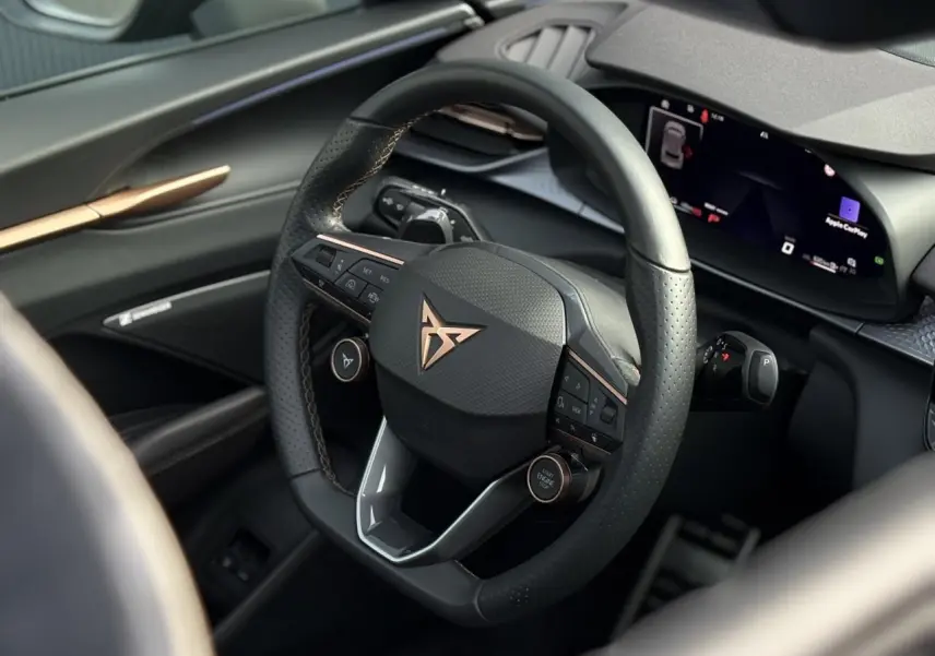 Vue rapprochée du volant cuir noir perforé avec logo cuivré et tableau de bord numérique du CUPRA Terramar 2024.