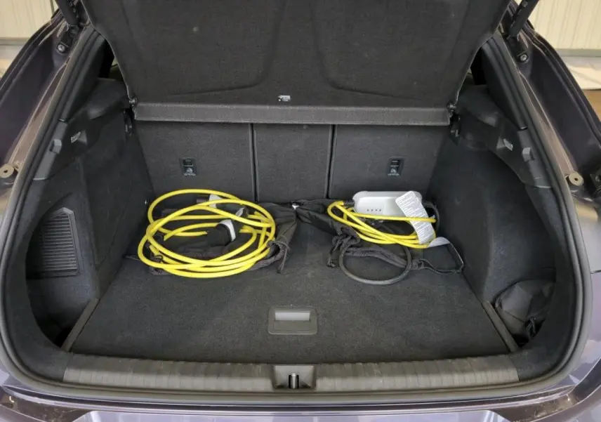 Coffre ouvert du CUPRA TERRAMAR 2024 Dark Void avec câble de recharge jaune visible sur la moquette noire.