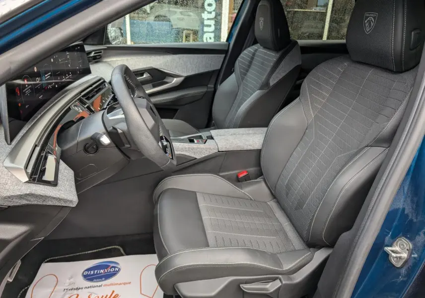 Vue intérieure côté conducteur du Peugeot 3008 Hybrid 2025 bleu métallisé, avec sièges tissu et cuir gris et tableau de bord numérique.