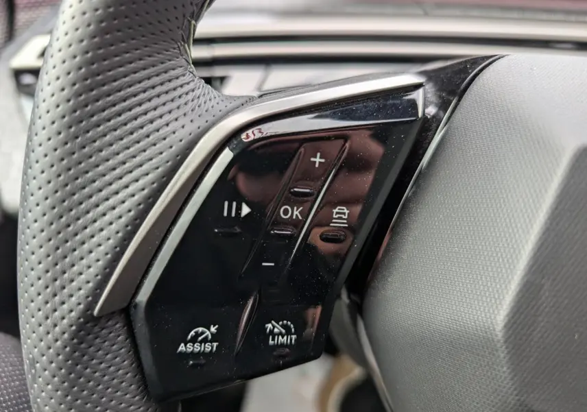 Gros plan sur les commandes noires du volant perforé côté gauche du Peugeot 3008 GT bleu métallisé 2025.