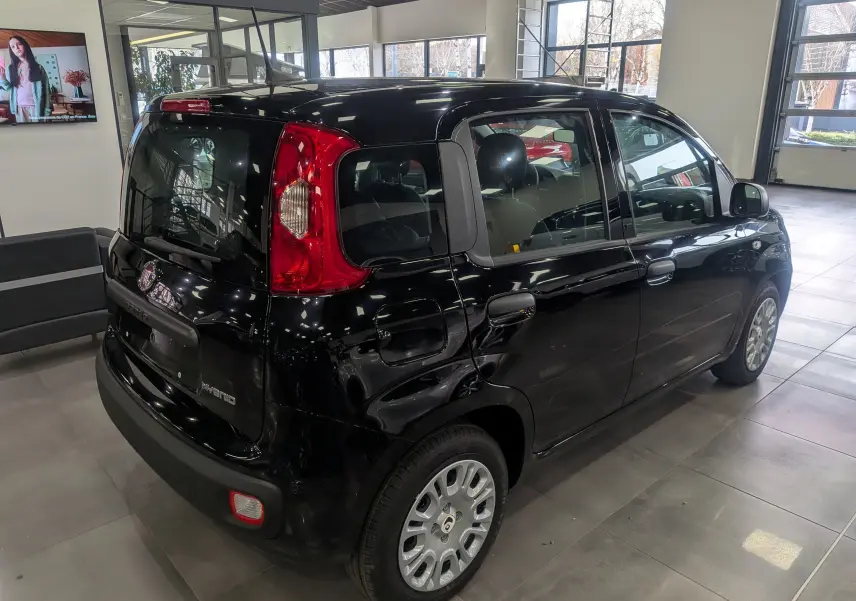 Vue 3/4 arrière droite d'une Fiat Panda 1.0 Hybrid City noire, avec feux arrière rouges et jantes argentées en showroom.
