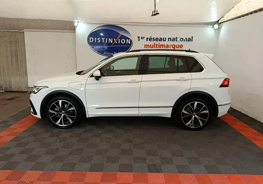 Vue de profil côté gauche d’un Volkswagen Tiguan blanc 2023 hybride rechargeable avec jantes alliage noires et toit ouvrant.