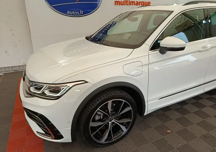 Vue 3/4 avant droit du Volkswagen Tiguan blanc hybride rechargeable avec jantes alliage noires et détails R-Line.