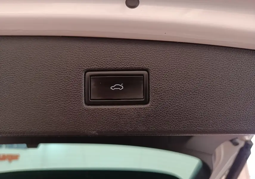Gros plan sur le bouton d'ouverture électrique du coffre, intérieur du hayon blanc du Volkswagen Tiguan hybride 2023.