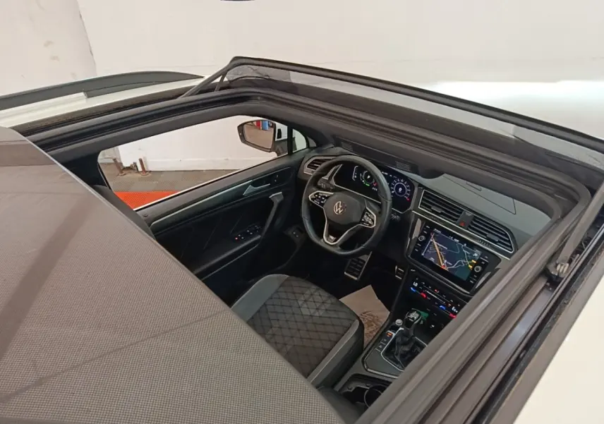 Vue intérieure par le toit ouvrant du Volkswagen Tiguan blanc, mettant en valeur le tableau de bord digital et le volant multifonctions.