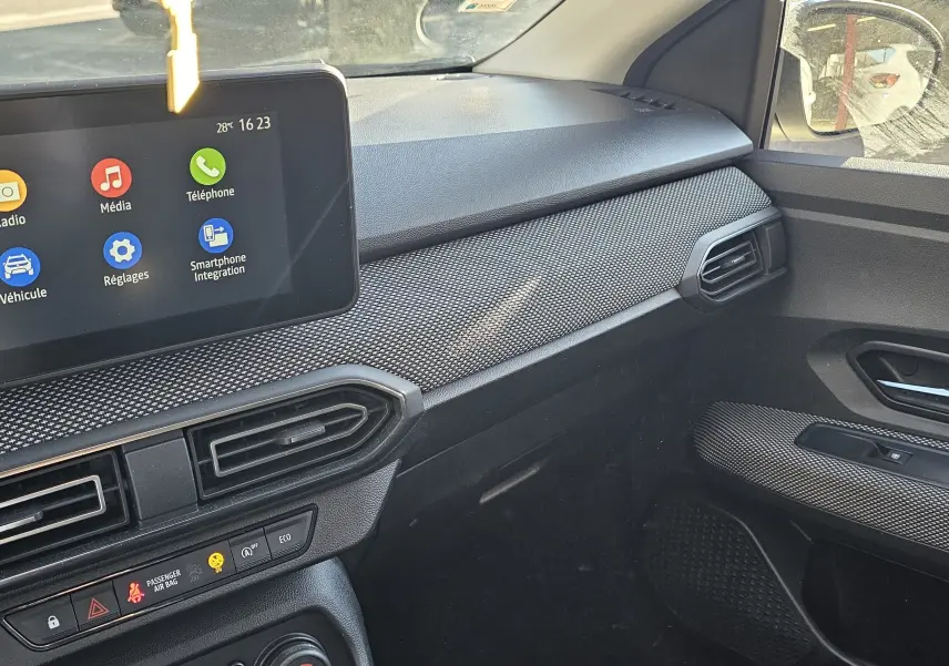 Intérieur de la Dacia Sandero III 2022 côté passager, tableau de bord noir avec écran tactile central et aérateurs hexagonaux.