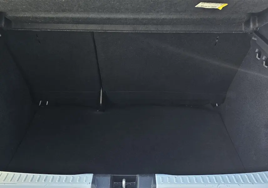 Coffre ouvert d'une Dacia Sandero III blanc glacier, montrant l'espace de chargement vide et les finitions intérieures noires.