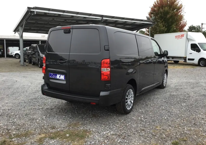 Vue 3/4 arrière droite d’un Peugeot Expert cabine approfondie gris titane avec vitres arrière opaques sur un parking.