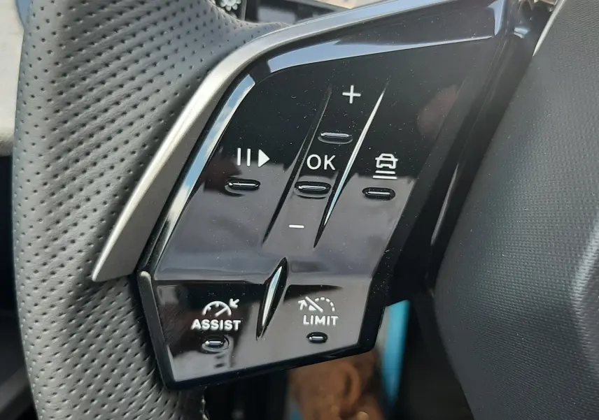 Gros plan sur les commandes au volant perforé du Peugeot 3008 Bleu Obsession, version hybride 2026, avec boutons multifonctions.