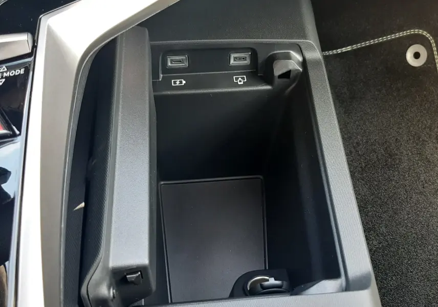 Gros plan sur la console centrale du Peugeot 3008 Hybrid 2026, montrant les ports USB et l'espace de rangement intérieur.