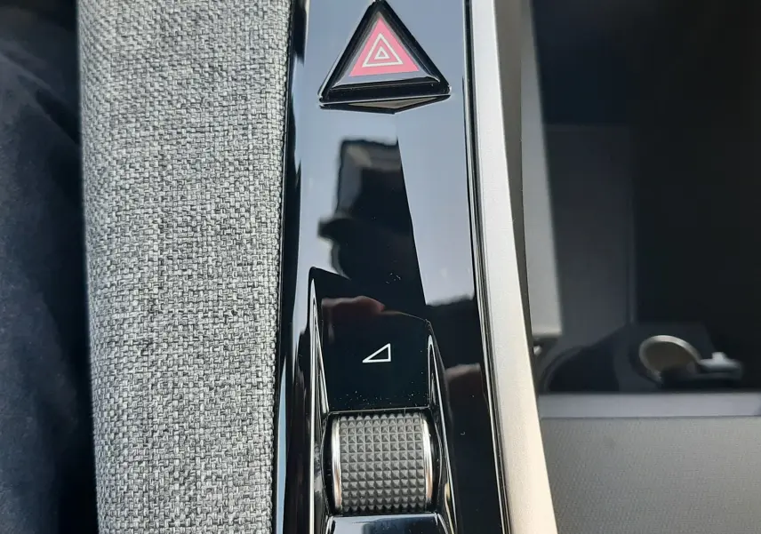 Gros plan sur la console centrale noire brillante du Peugeot 3008 1.2 Hybrid 145ch GT, avec bouton triangle rouge d’alerte.