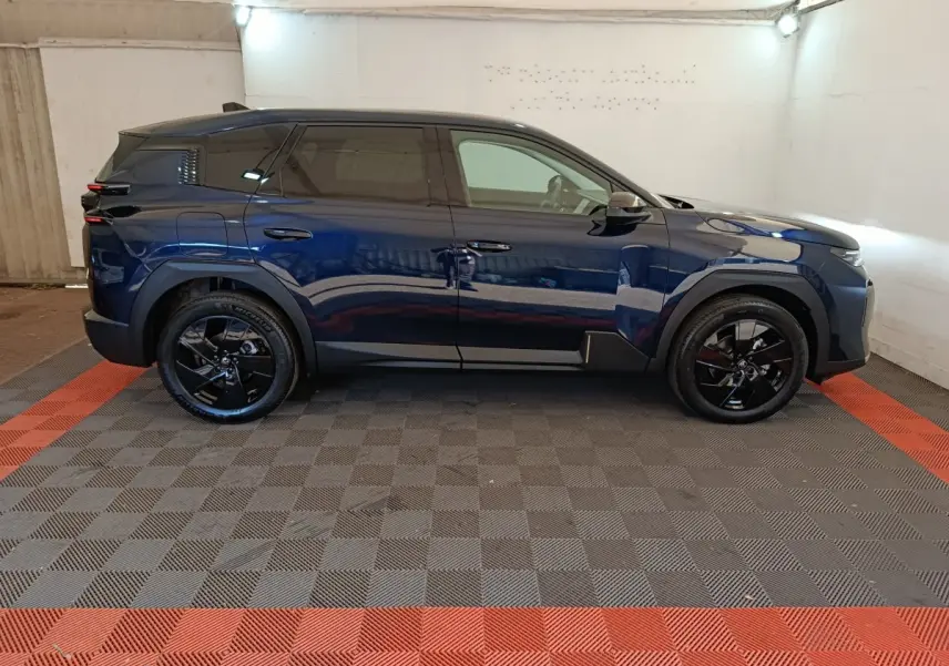 Vue latérale droite d'une Citroën C5 hybride bleu foncé avec jantes noires dans un garage éclairé.