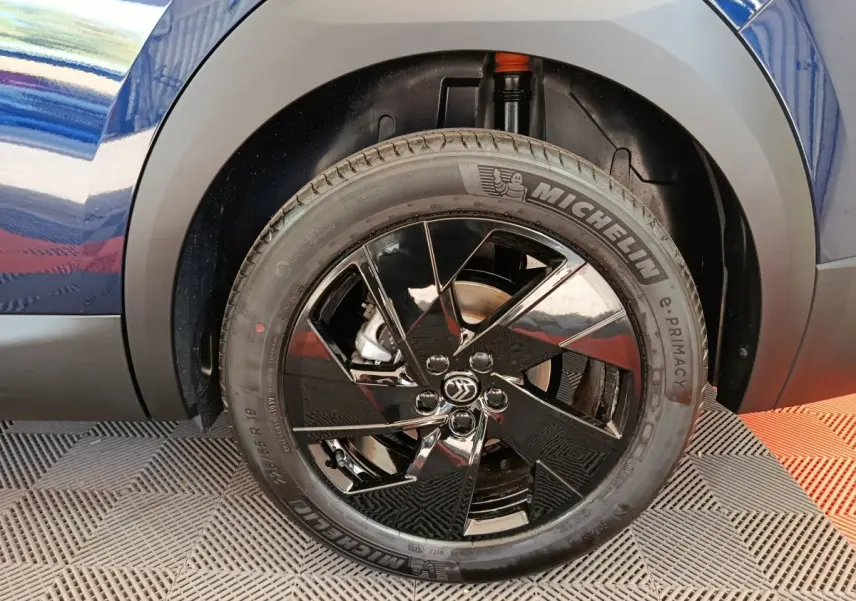 Gros plan sur la roue avant gauche noire brillante d'une Citroën C5 hybride bleue, avec pneu Michelin visible.
