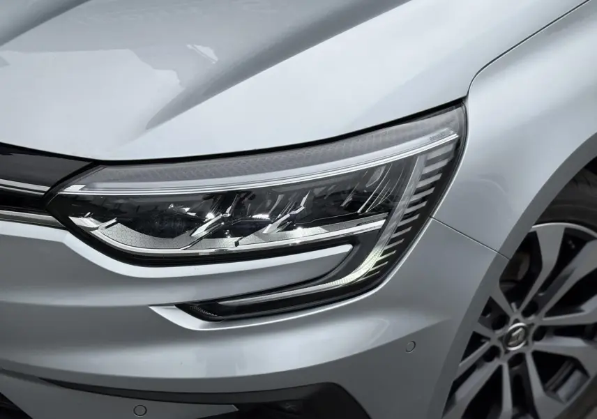 Gros plan sur le phare avant droit et la jante alliage gris d'une Renault Mégane Break 2024 gris Highland