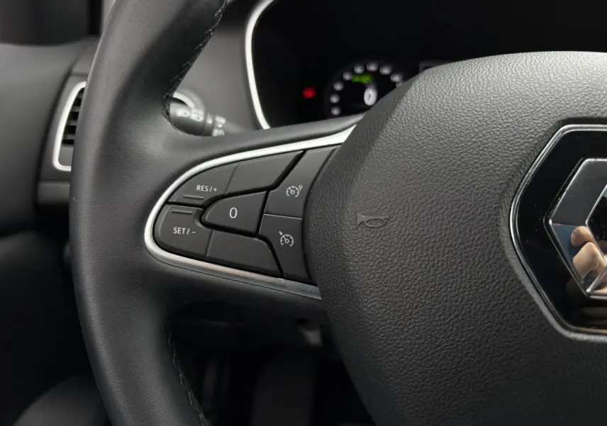 Gros plan sur le volant noir de la Renault Mégane Break 2024, avec commandes de régulateur de vitesse visibles à gauche.