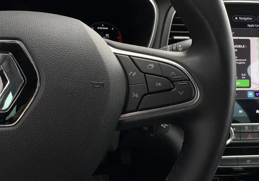 Gros plan sur le volant noir de la Renault Mégane Break 2024 avec commandes intégrées et écran tactile GPS visible.