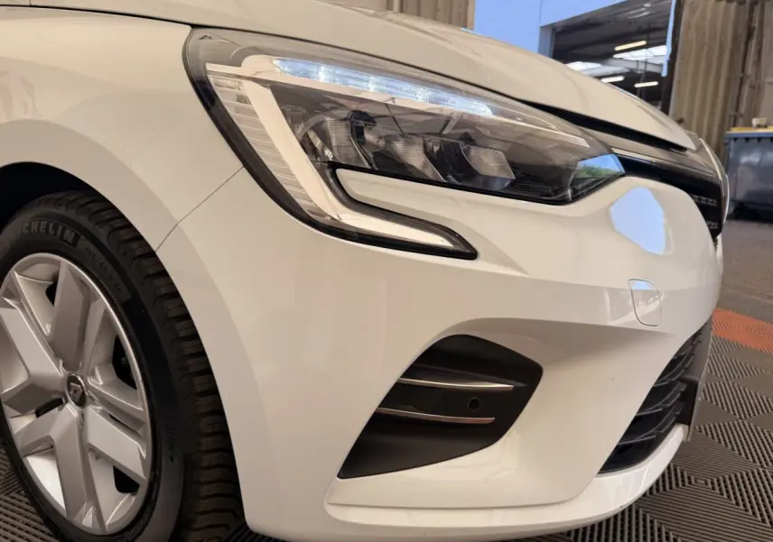 Gros plan sur l'avant droit blanc d'une Renault Clio Business E-Tech hybride 2022, mettant en valeur le phare LED et la jante.