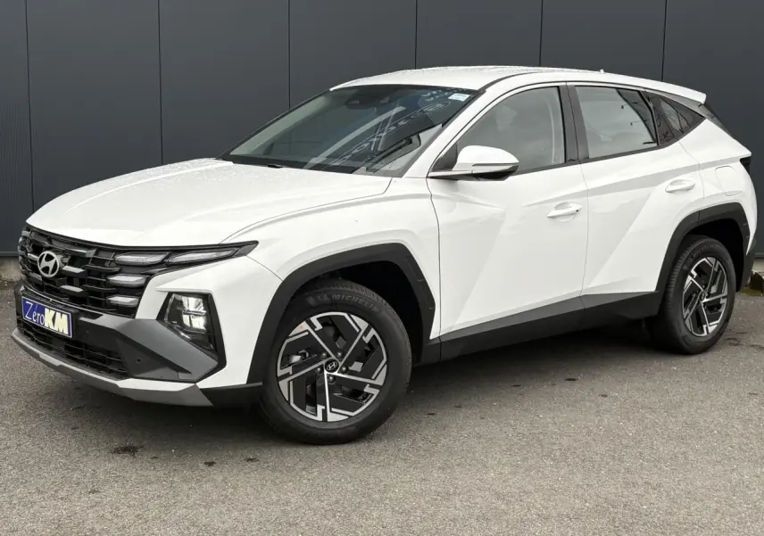 Hyundai Tucson blanc Atlas en 3/4 avant droit, avec jantes alliage et calandre noire distinctive.