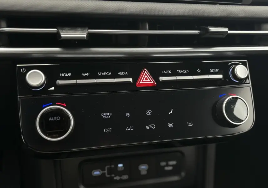 Gros plan sur la console centrale noire du Hyundai Tucson blanc Atlas 2026, montrant les commandes de climatisation et multimédia.