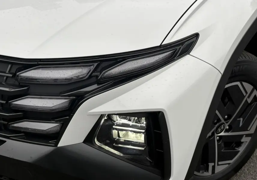 Gros plan sur l'avant droit blanc Atlas du Hyundai Tucson 2026, mettant en valeur les phares bi-LED et la jante alliage.