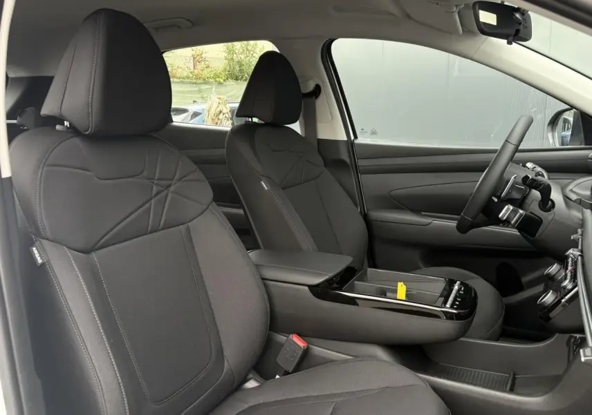 Vue intérieure côté conducteur du Hyundai Tucson 2026, sièges tissu noir et console centrale avec accoudoir.