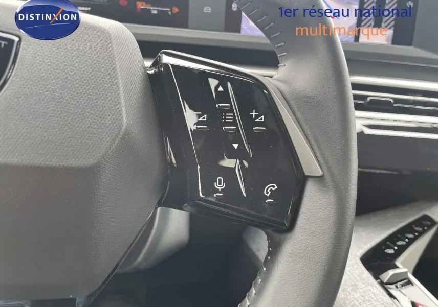 Gros plan sur les commandes gauche du volant cuir noir du Peugeot 5008 gris Artense 2025, tableau de bord en arrière-plan.