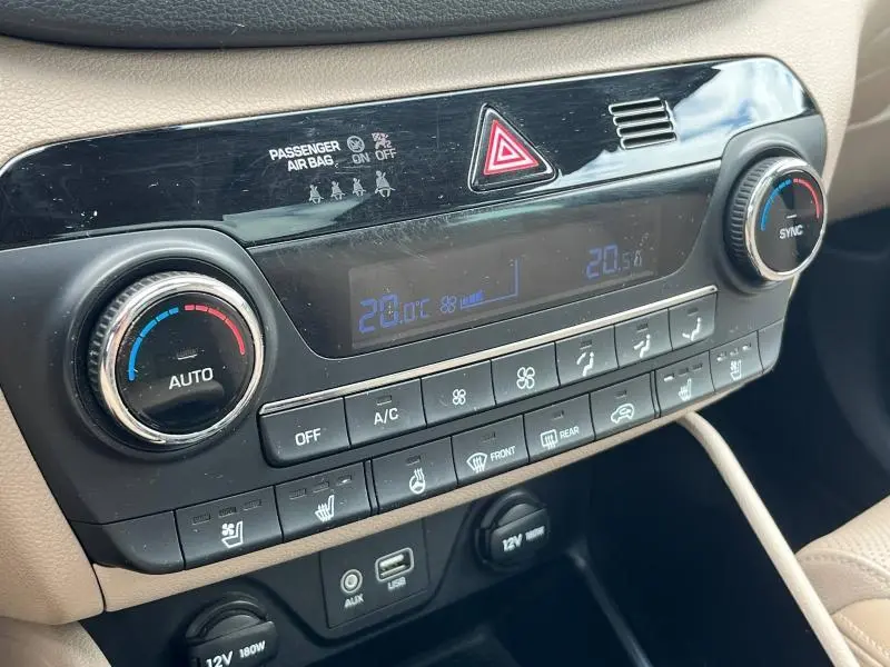 Gros plan sur la console centrale du Hyundai Tucson 2017, montrant les commandes de climatisation et les prises USB et 12V.