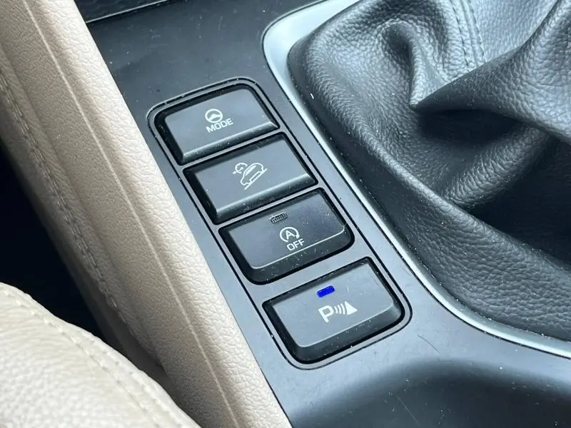 Gros plan sur les commandes du mode de conduite et assistance au stationnement dans l'habitacle beige du Hyundai Tucson blanc.