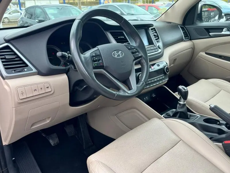 Vue intérieure côté conducteur du Hyundai Tucson 2017 avec cuir beige, volant multifonction en cuir et boîte manuelle.