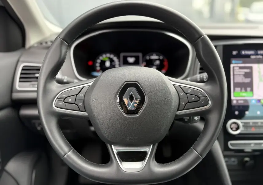 Volant en cuir noir avec logo Renault au centre, tableau de bord numérique et écran tactile GPS en arrière-plan.