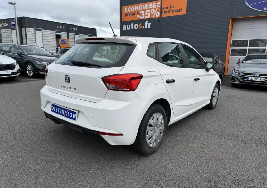 Vue 3/4 arrière droite d'une SEAT Ibiza blanche Candy 2019 avec jantes enjoliveurs et feux arrière rouges.