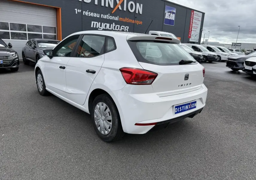 Vue 3/4 arrière droite d'une SEAT Ibiza blanche Candy 2019 avec jantes acier et enjoliveurs sur parking extérieur.