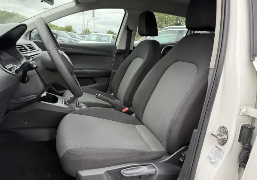 Vue intérieure côté conducteur de la SEAT Ibiza blanche, montrant les sièges avant gris et le volant multifonction.