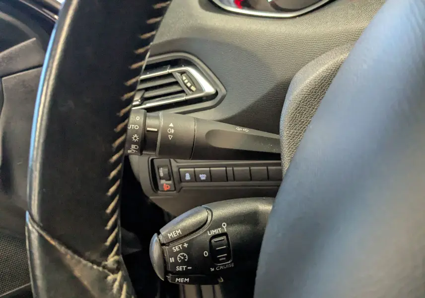 Gros plan sur la commande de régulateur de vitesse et le commodo d’éclairage à gauche du volant d’une Peugeot 308 noire.