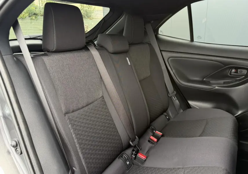 Vue latérale des sièges arrière gris foncé de la Toyota Yaris Cross 2026 avec ceinture de sécurité et porte noir mat.