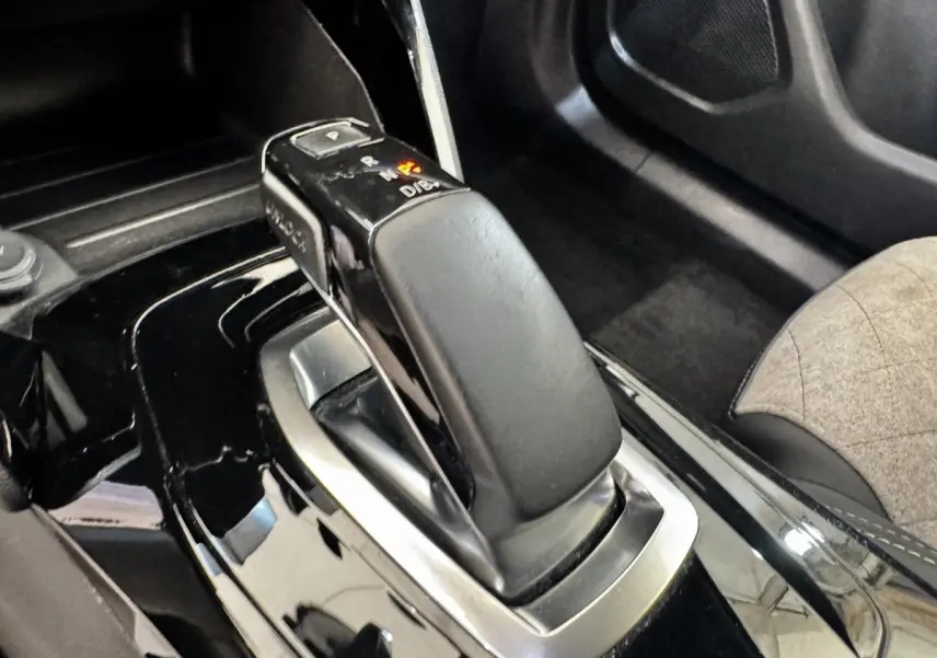 Gros plan sur la commande de boîte automatique noire brillante du Peugeot E-2008 électrique GT Pack, intérieur tissu gris.