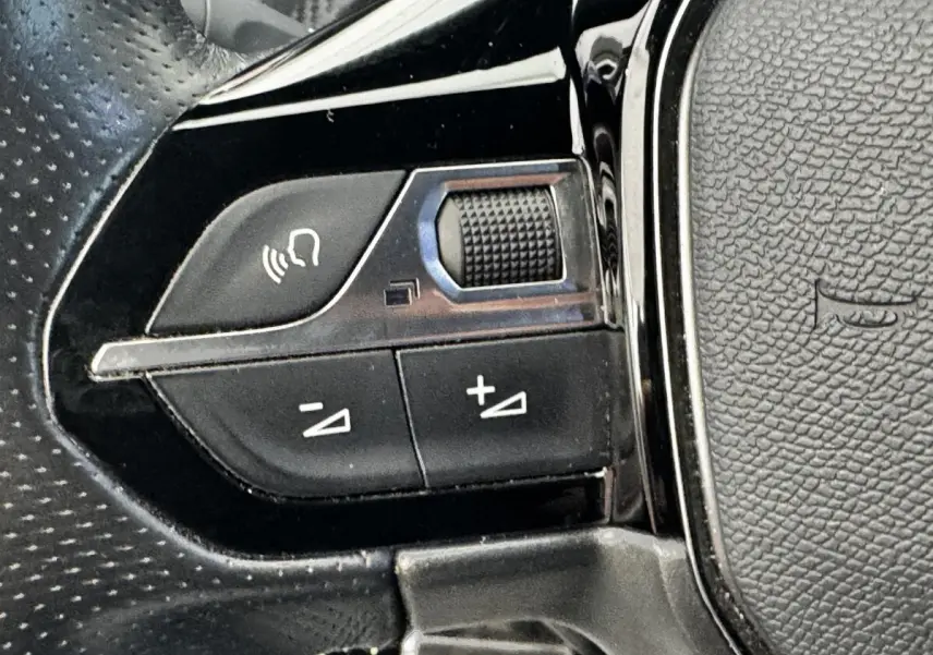 Gros plan sur les commandes multifonctions du volant cuir noir du Peugeot E-2008 électrique GT Pack 2021.