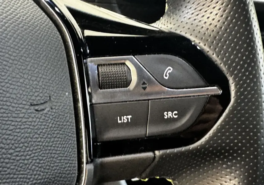 Gros plan sur les commandes multifonctions gauche du volant cuir perforé noir du Peugeot E-2008 électrique GT Pack 2021.