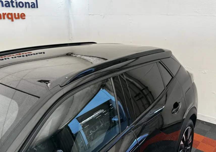 Vue 3/4 arrière côté gauche d’un Peugeot E-2008 électrique GT Pack noir avec vitres teintées et barres de toit noires.