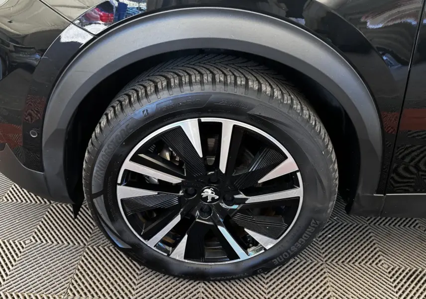 Gros plan sur la roue avant gauche noire du Peugeot E-2008 électrique GT Pack avec jante alliage bicolore.