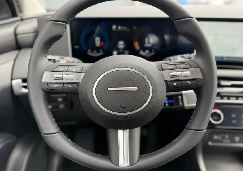 Gros plan sur le volant noir du Hyundai Tucson 2026 avec commandes intégrées et tableau de bord numérique flou en arrière-plan.