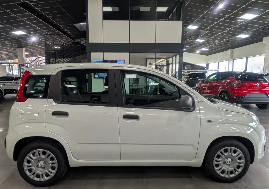 Vue de profil côté gauche d'une FIAT Panda 1.0 70 CH Hybrid City blanche Gelato en showroom, avec rétroviseurs noirs et jantes acier.