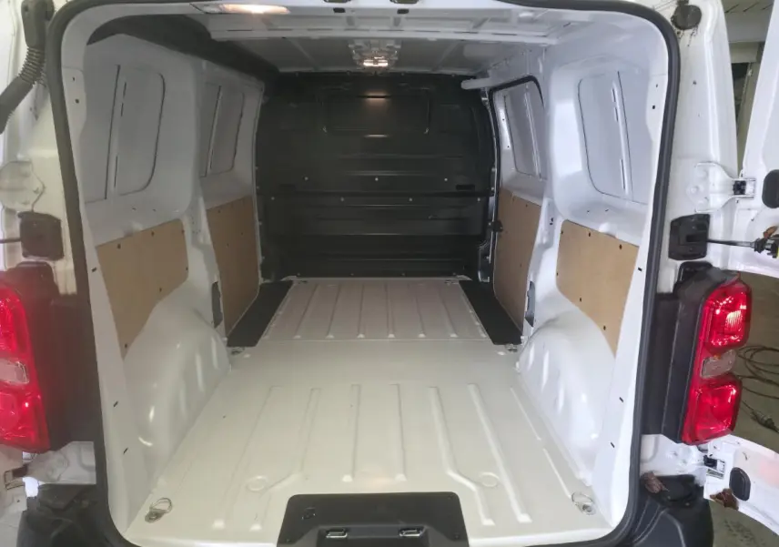 Vue intérieure arrière du fourgon blanc Opel Vivaro 2025, montrant l'espace de chargement vide avec panneaux latéraux en bois.