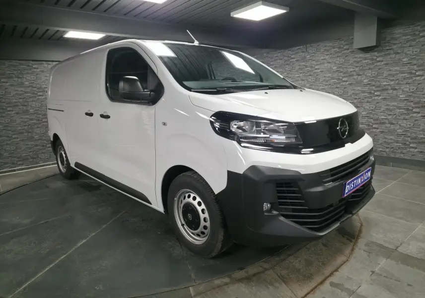 Opel Vivaro blanc en 3/4 avant droit, avec calandre noire et pare-chocs avant noir mat dans un intérieur gris.