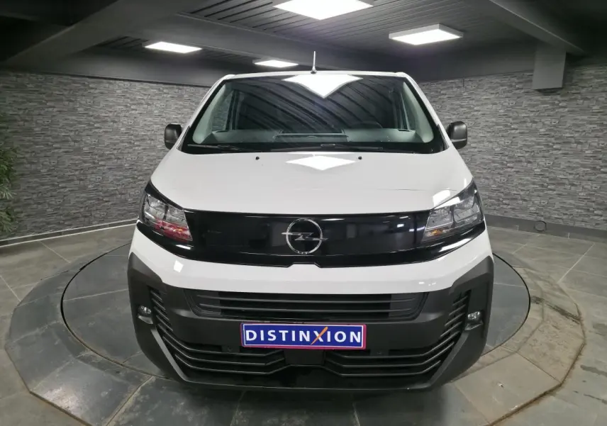 Vue frontale d'un Opel Vivaro blanc 2025 avec calandre noire et projecteurs intégrés, en showroom intérieur.
