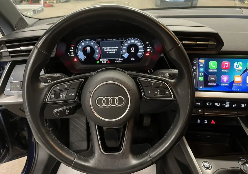 Vue intérieure centrée sur le volant noir d'une Audi A3 Sportback 2021 avec tableau de bord numérique et écran tactile CarPlay.